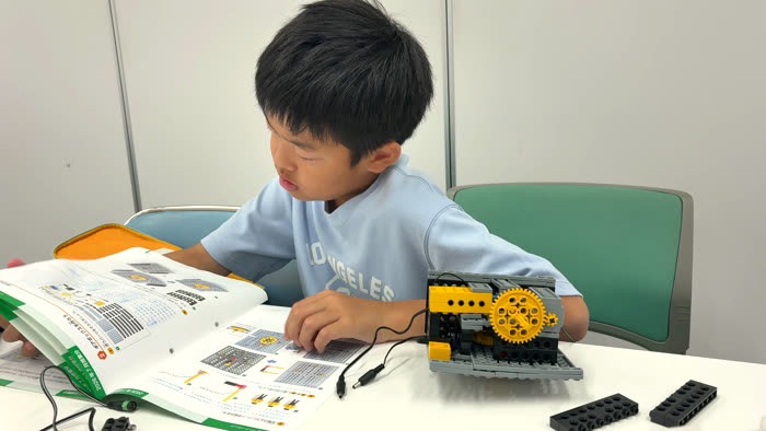 テキストを見ながらロボットに手を伸ばす生徒